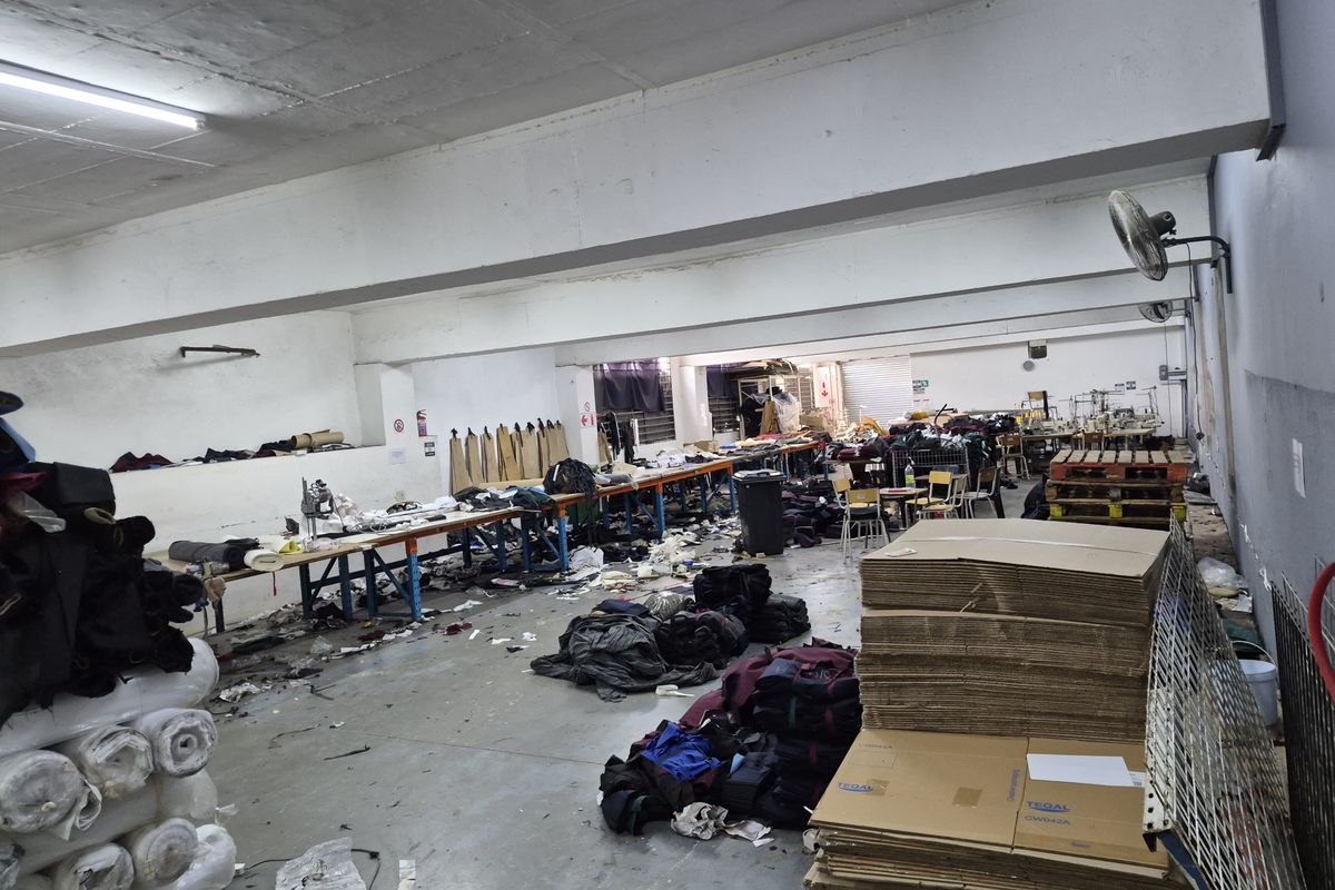 Industrial workspace featuring concrete flooring, exposed structural beams, and overhead fluorescent lighting, currently utilized for manufacturing or storage operations.