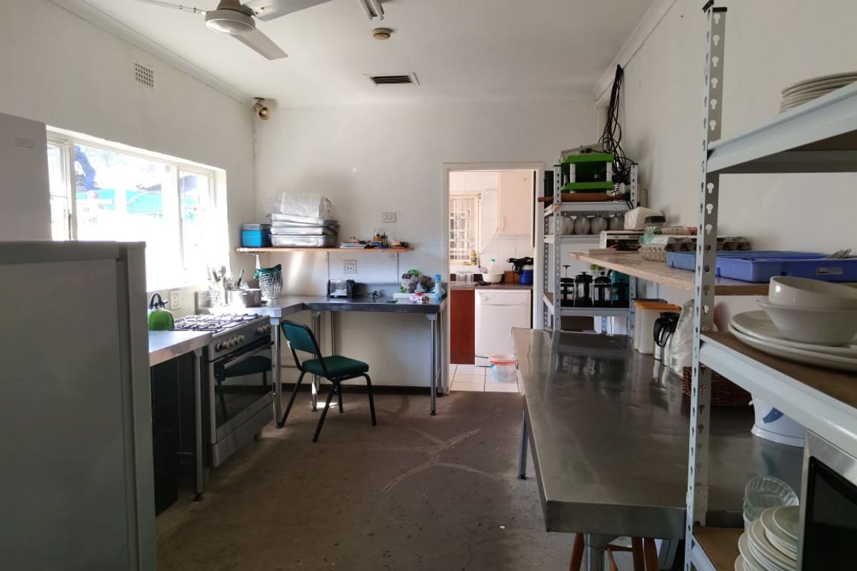 A functional commercial-style kitchen featuring stainless steel work surfaces, a gas stove, and an adjacent scullery area with tiled flooring.