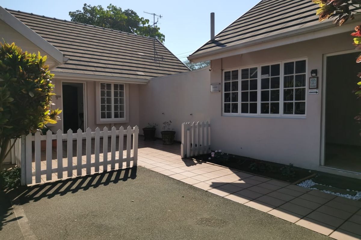 Exterior view of the guest house featuring tiled walkways, white picket fencing, and multiple building entrances with classic window frames.