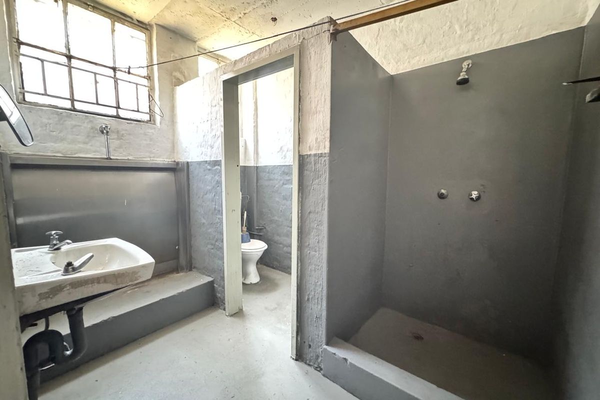 Industrial-style bathroom featuring a walk-in shower, wall-mounted basin, and separate toilet area with exposed brick walls and concrete flooring.