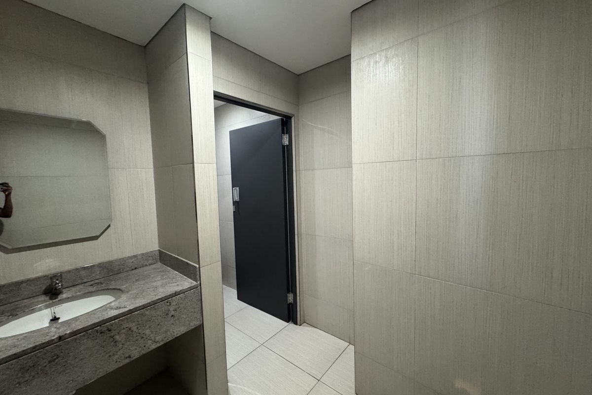 A modern office restroom featuring neutral wall tiling, a granite vanity countertop with an integrated basin, and a dark-toned door.