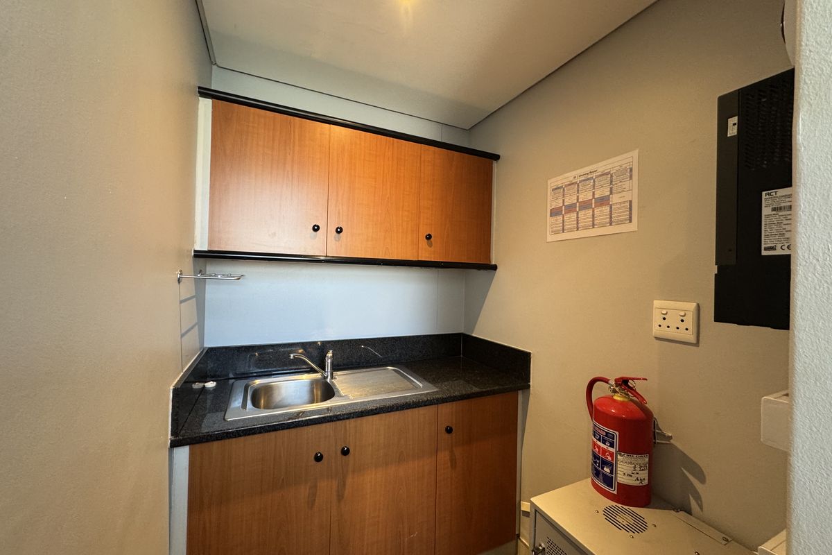 A compact office kitchenette featuring wood-finish cabinetry, a stainless steel sink, and dark stone-look countertops.