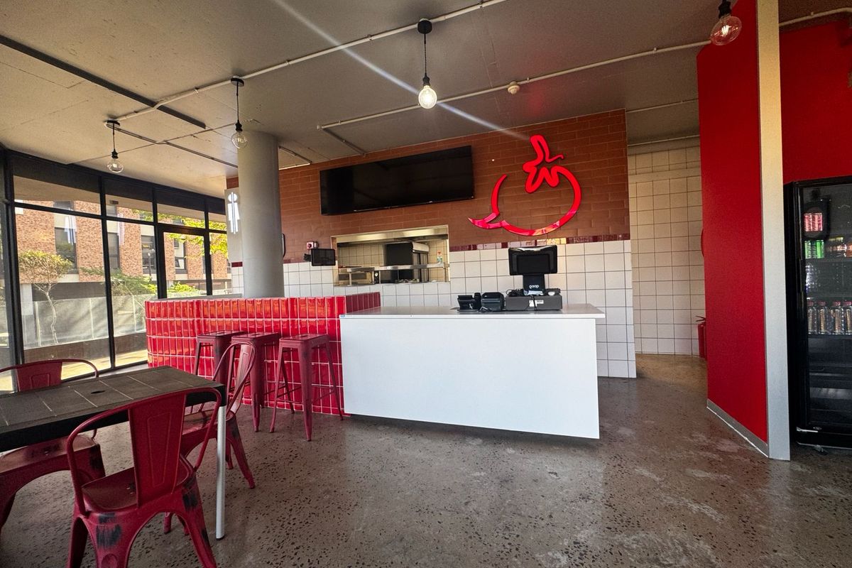 Modern retail space featuring a service counter, polished concrete floors, exposed ceiling, and vibrant red tiled accents, suitable for a cafe or restaurant setup.