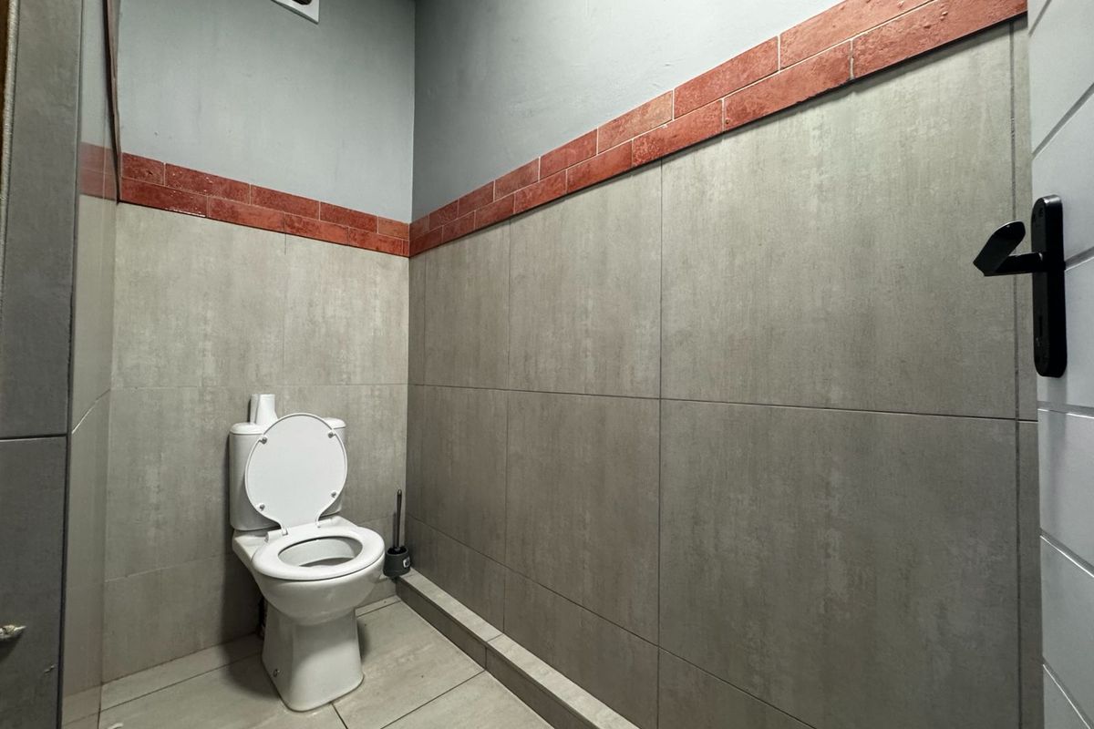 A functional bathroom featuring grey tiled walls with a decorative red brick-style border, tiled flooring, and a wall-mounted extractor fan.
