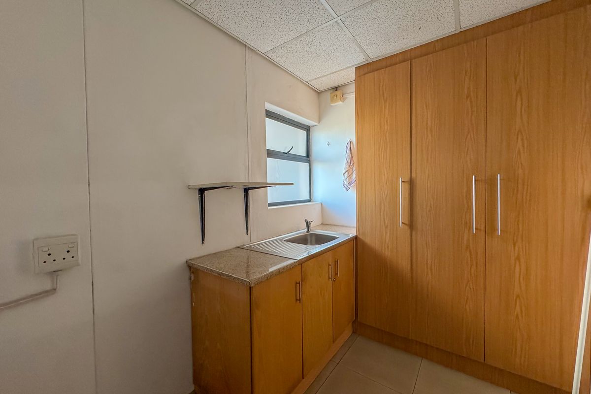 A functional kitchenette area featuring wood-finish cabinetry, a stainless steel sink with granite countertop, and a drop ceiling.