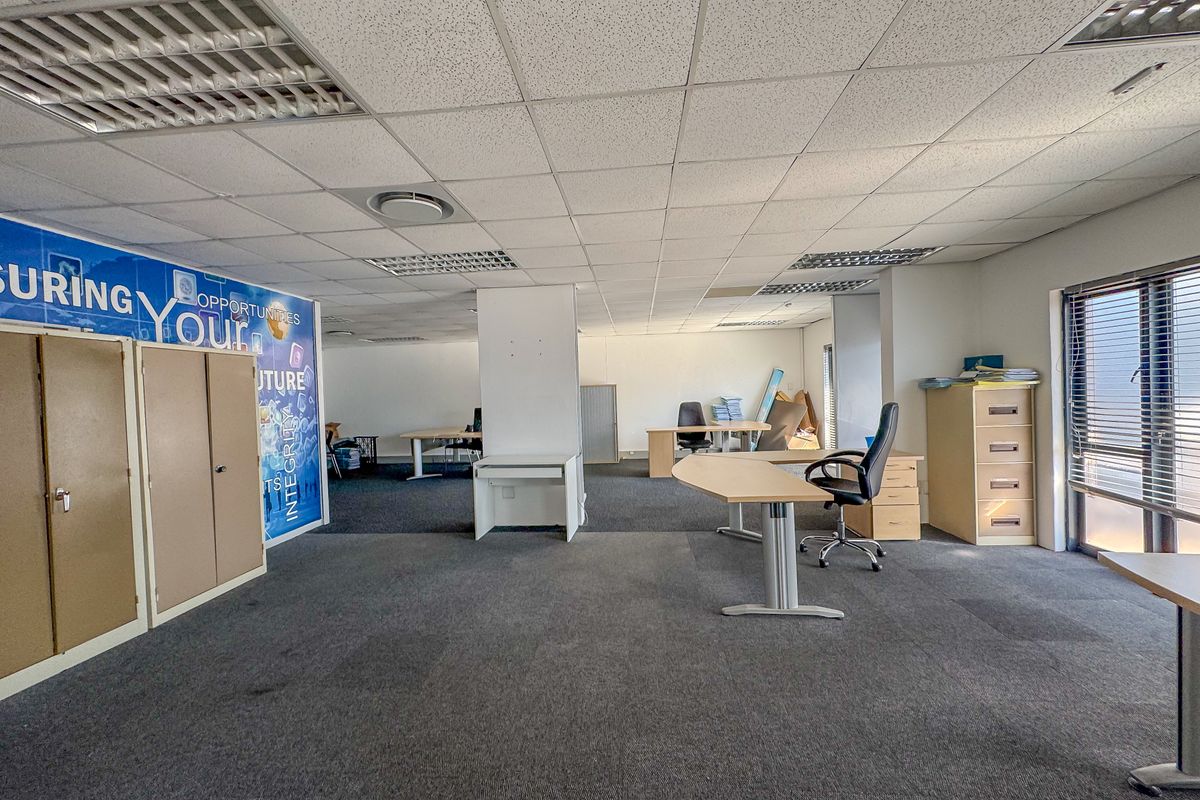 Open-plan office space featuring suspended ceilings, recessed lighting, carpeted flooring, and large windows with blinds, offering a functional workspace environment.