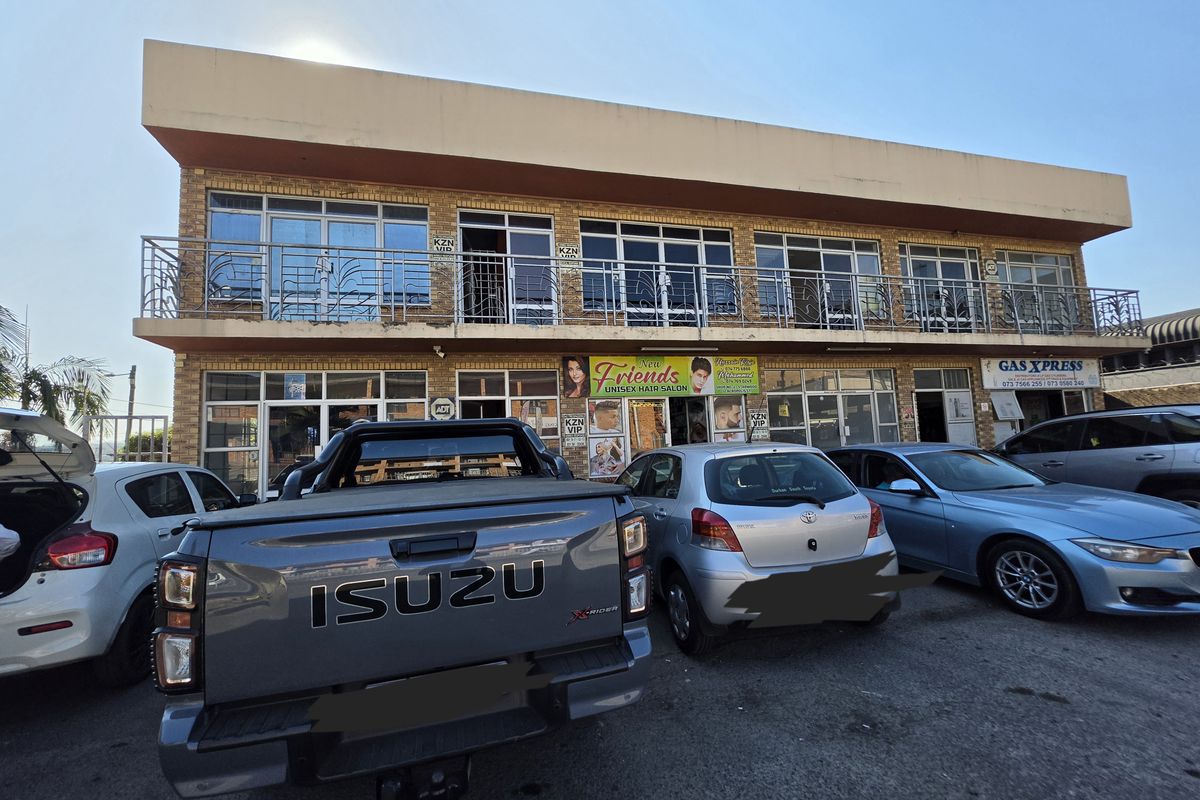Front elevation of a two-story commercial building featuring brick facade, upper-level balcony with metal railings, and ground-floor retail storefronts with parking.