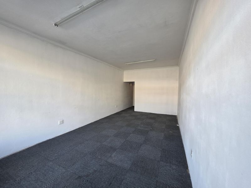 An empty commercial office space featuring grey carpet tiles, plain white walls, and overhead fluorescent lighting, ready for custom fit-out.