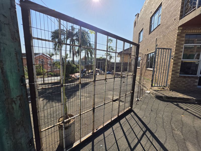 Rear exterior view of a commercial property featuring a paved yard, wire mesh fencing, and brick building facade.