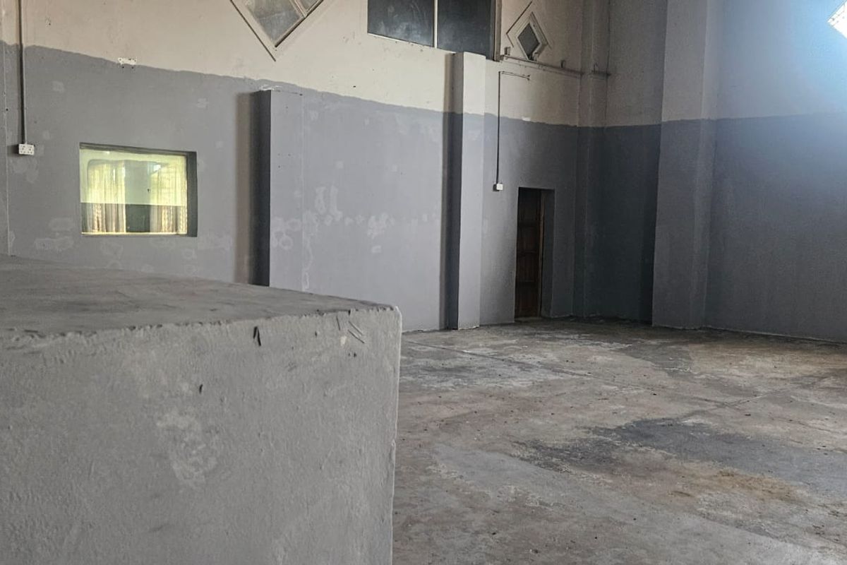 An expansive, empty industrial utility space featuring concrete flooring, high-level windows, and painted masonry walls, suitable for various commercial or storage applications.