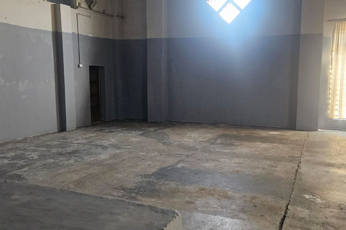 Spacious industrial utility area featuring high ceilings, exposed structural columns, and worn concrete flooring, offering a versatile blank canvas for various commercial or storage uses.