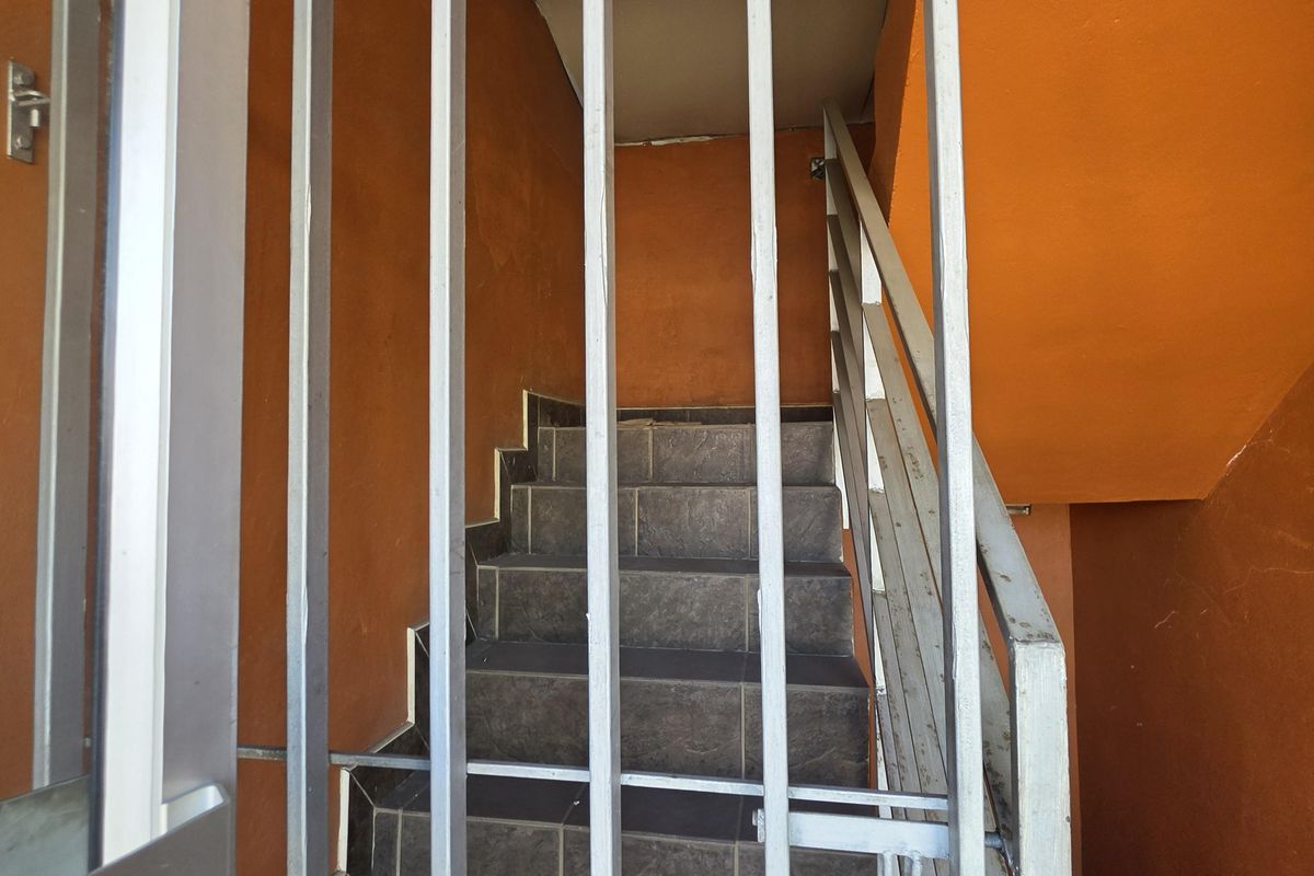 A functional staircase area featuring tiled steps, a metal security gate, and a handrail, finished with orange painted walls.
