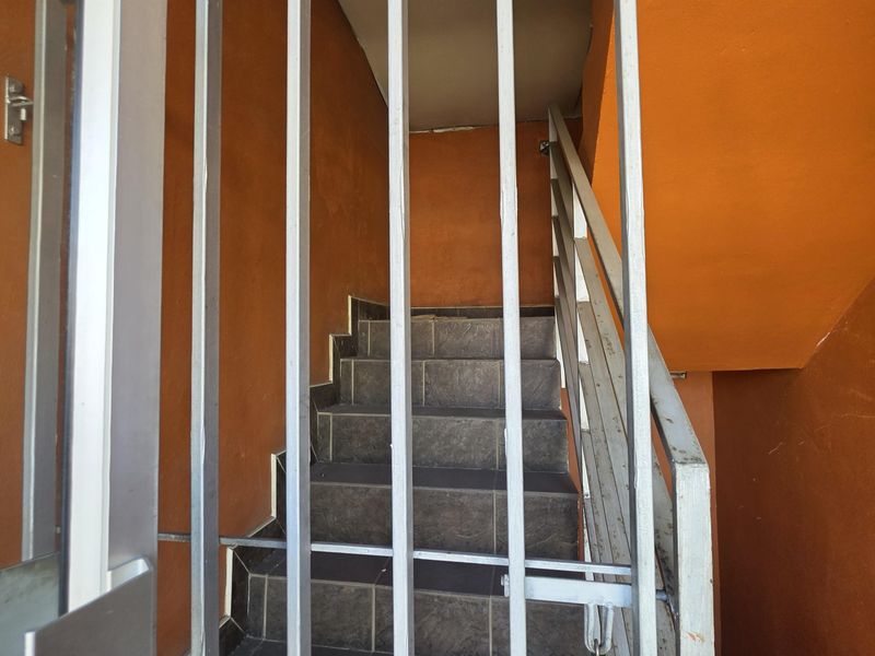 A functional staircase area featuring tiled steps, a metal security gate, and a handrail, finished with orange painted walls.