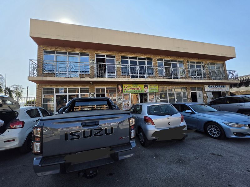 Front elevation of a two-story commercial building featuring brick facade, upper-level balcony with metal railings, and ground-floor retail storefronts with parking.