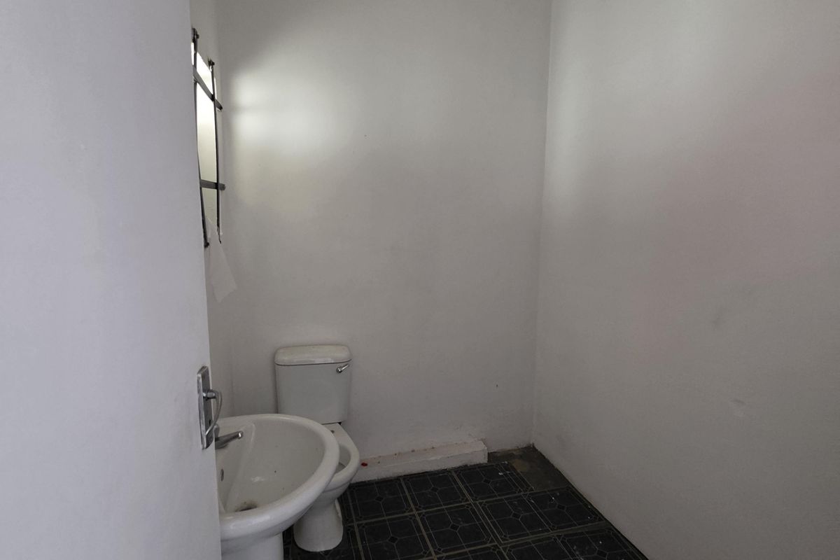 A compact, empty bathroom featuring a pedestal basin and toilet with dark tiled flooring, requiring cosmetic updates and repairs to finishes.