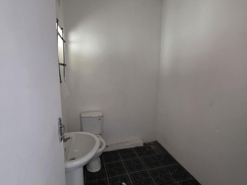 A compact, empty bathroom featuring a pedestal basin and toilet with dark tiled flooring, requiring cosmetic updates and repairs to finishes.