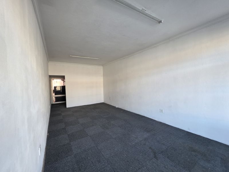 An empty, open-plan office space featuring grey carpet tiles, white walls, and overhead fluorescent lighting, suitable for a variety of commercial uses.