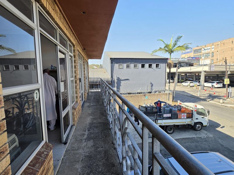 An exterior balcony featuring a metal balustrade and brick facade, overlooking a commercial street area.