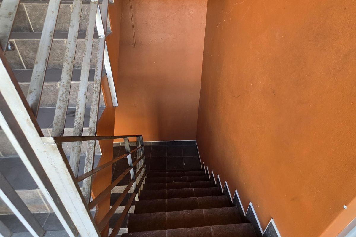 A functional stairwell featuring tiled steps and a metal handrail, showing signs of wear and requiring maintenance.