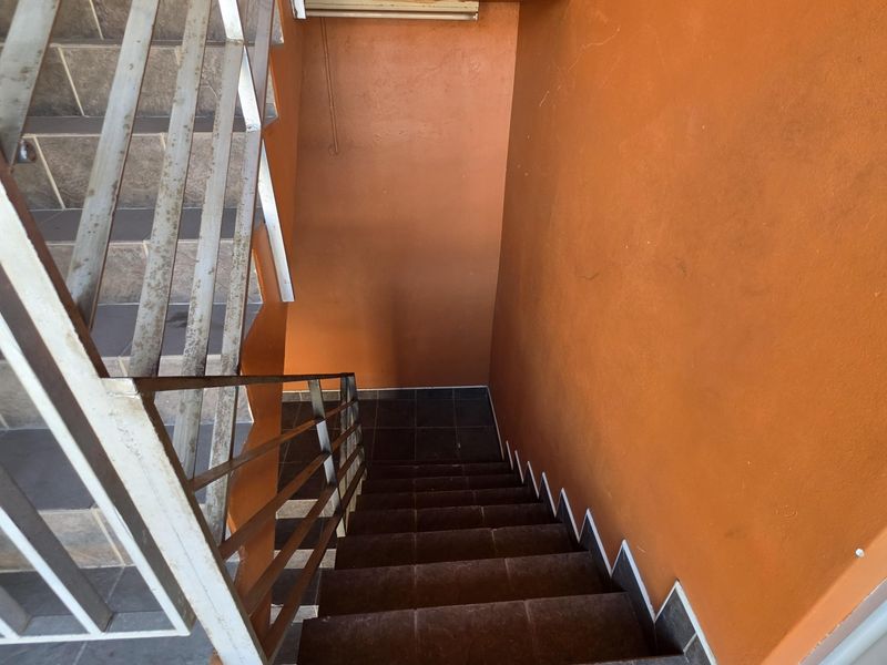 A functional stairwell featuring tiled steps and a metal handrail, showing signs of wear and requiring maintenance.