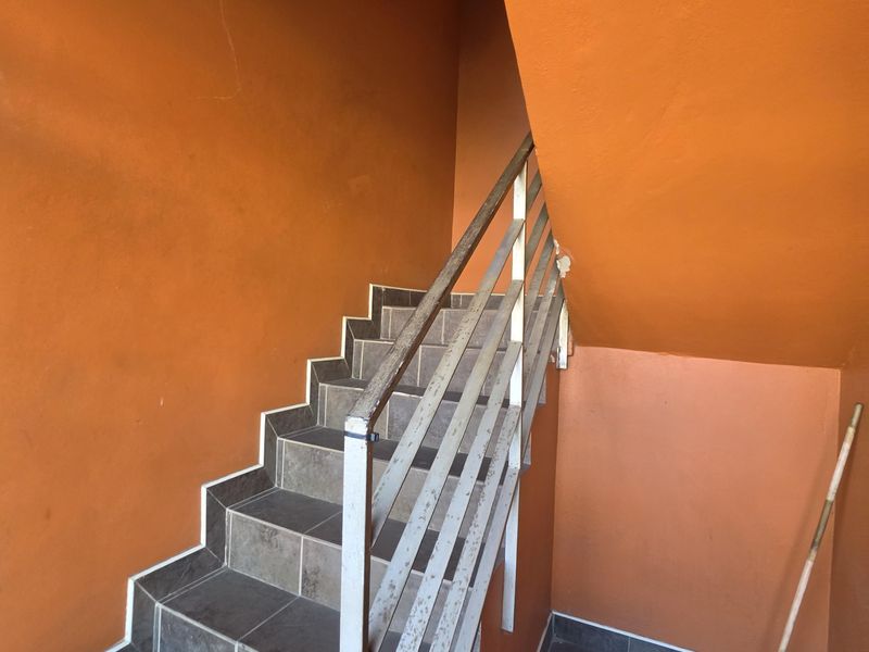 A functional interior staircase featuring tiled steps and a metal handrail, set against vibrant orange painted walls.