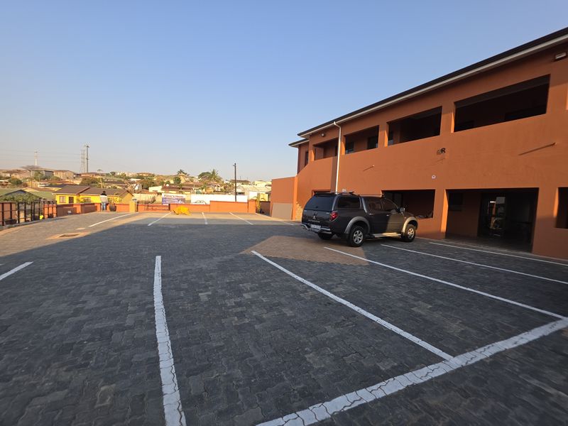 A paved parking area with marked bays situated in front of a multi-level commercial or residential building.