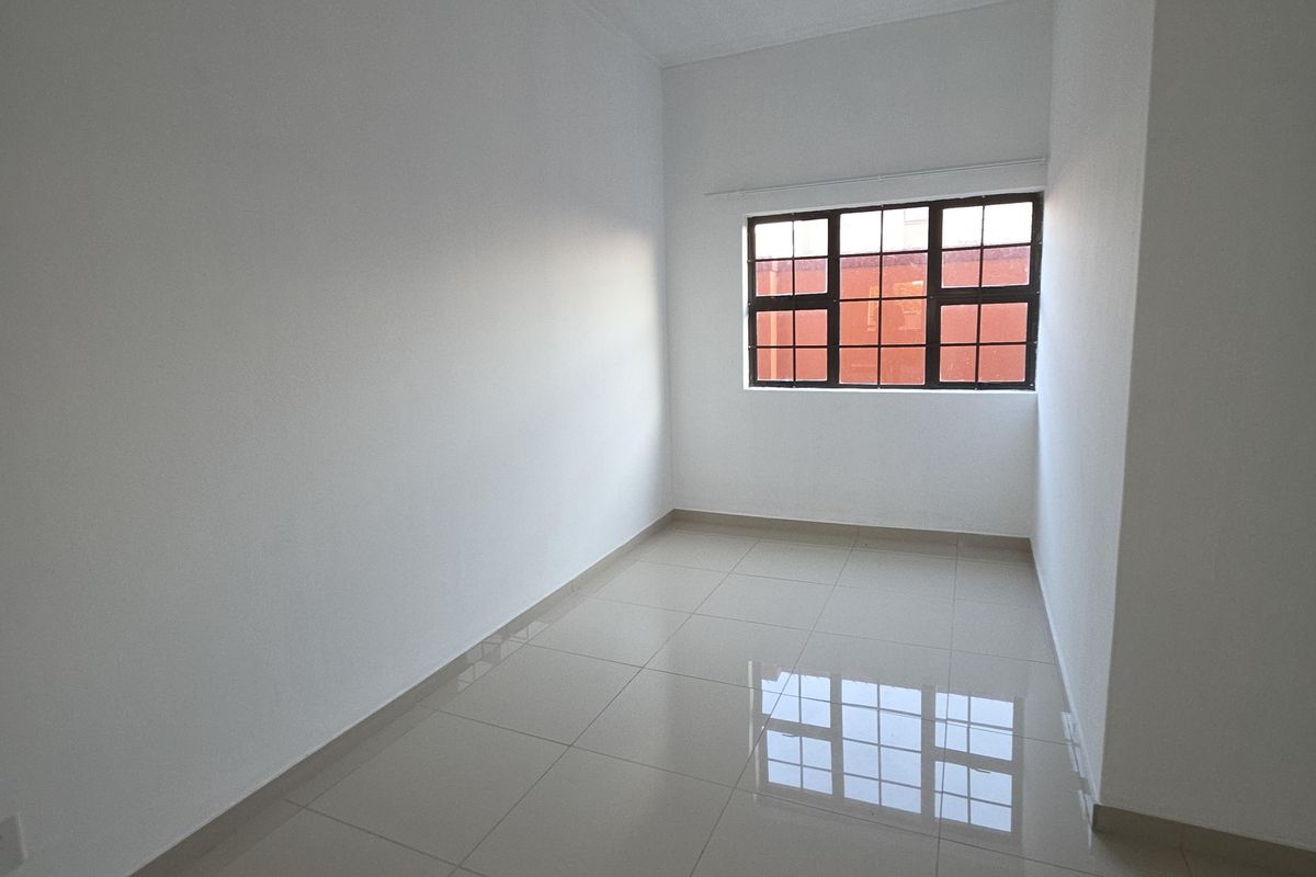 A bright, empty bedroom featuring neutral tiled flooring and a grid-pattern window, providing a clean and versatile space ready for personalization.