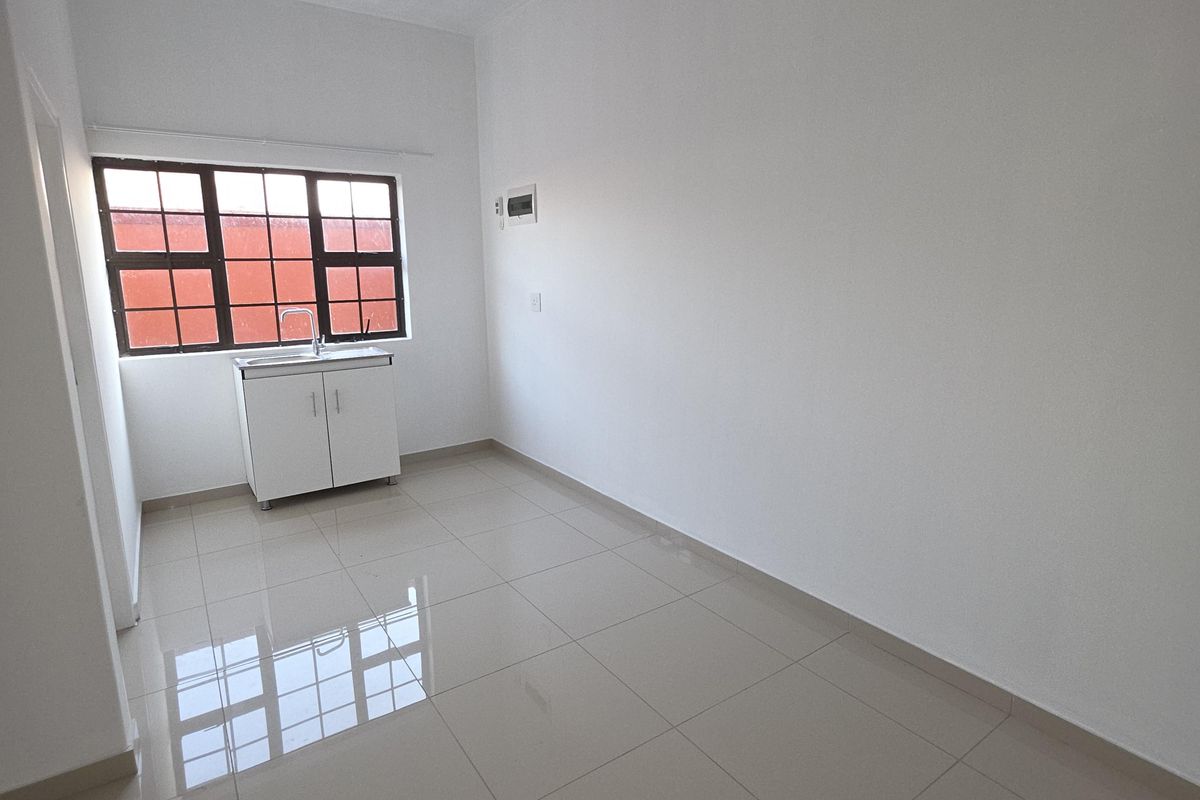 A clean, empty kitchen area featuring tiled flooring, a single basin sink with base cabinetry, and large windows with security bars.