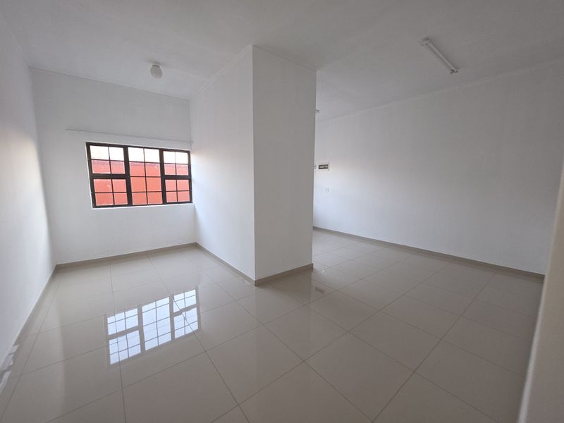 A bright, empty living area featuring neutral tiled flooring, white walls, and a large grid-pattern window providing natural light.