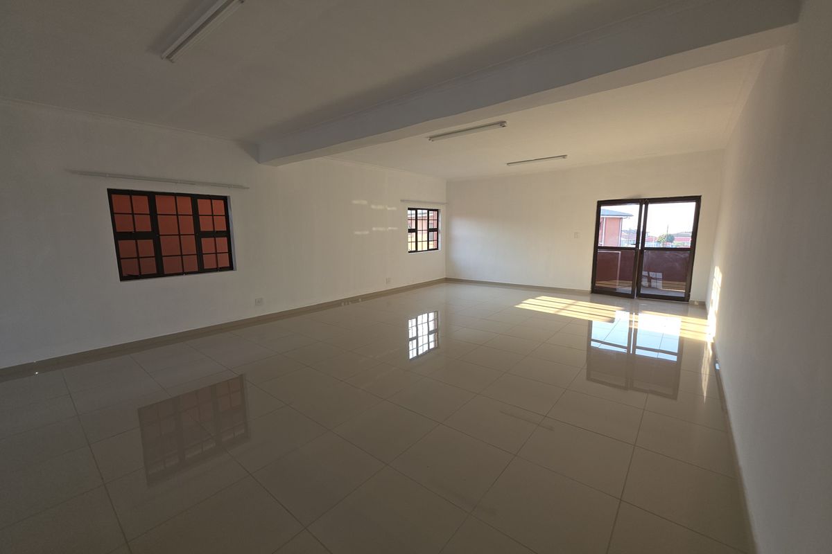 A spacious, empty living area featuring polished tiled flooring, neutral walls, and natural light through aluminium-framed windows and a sliding glass door.