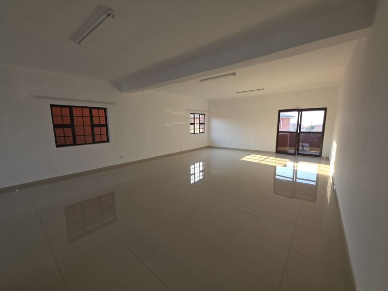 A spacious, empty living area featuring polished tiled flooring, neutral walls, and natural light through aluminium-framed windows and a sliding glass door.