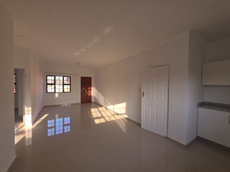 Bright and spacious open-plan living area featuring neutral tiled flooring, clean white walls, and a compact kitchen corner with granite countertops.
