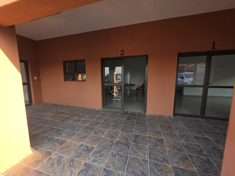 A covered patio area featuring tiled flooring and multiple aluminium-framed glass entrances, providing access to individual office or utility units.