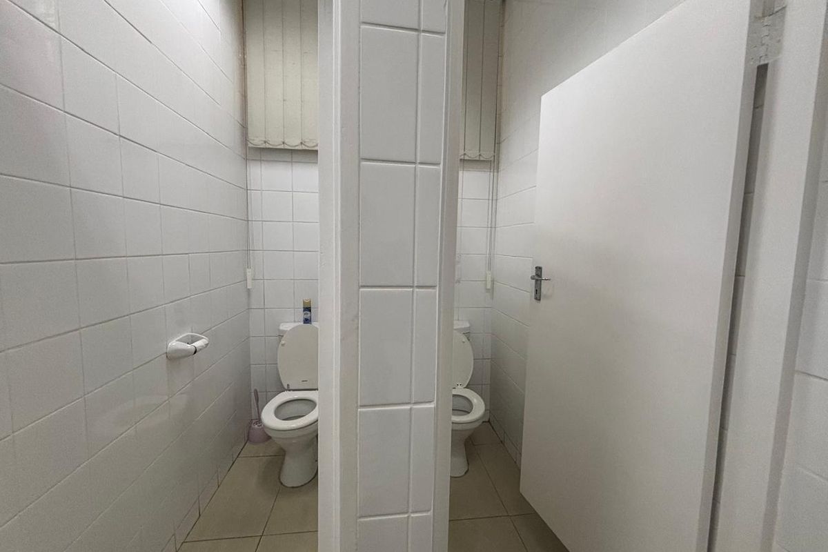 A functional commercial bathroom facility featuring two separate toilet stalls with tiled walls and flooring.
