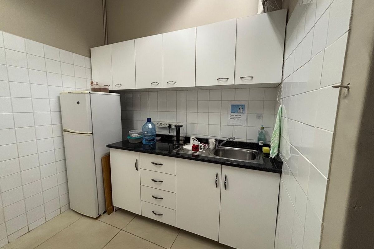 A functional kitchenette featuring white cabinetry, a black granite countertop, stainless steel sink, and full-height white wall tiling.