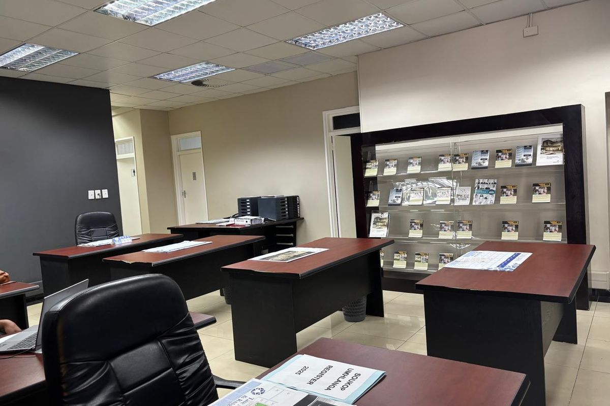 A professional office space featuring suspended ceilings with recessed lighting, tiled flooring, and a large built-in display shelving unit for brochures.