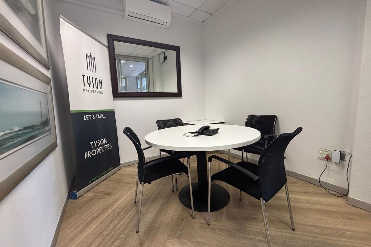 A compact commercial office space featuring laminate flooring, a suspended ceiling, and a wall-mounted air conditioning unit.