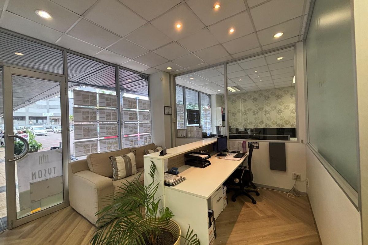 A professional commercial office space featuring modern herringbone flooring, glass partitions, and a suspended ceiling with recessed lighting, suitable for a reception or workspace.