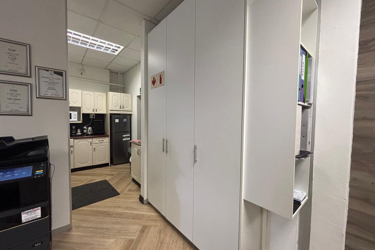 A functional commercial kitchenette area featuring built-in white cabinetry, laminate flooring, and integrated storage solutions, suitable for office staff use.