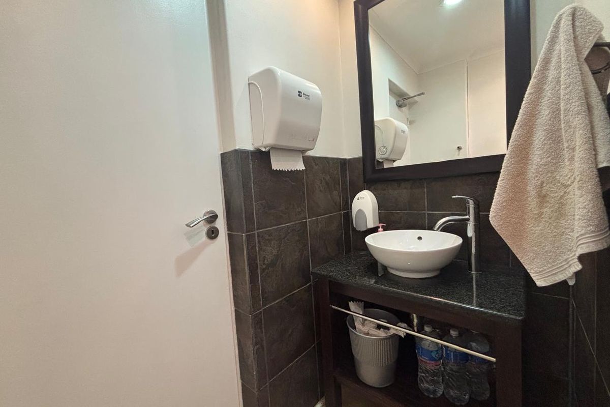 A compact commercial bathroom featuring a modern vessel sink, granite vanity countertop, and tiled splashback with wall-mounted utility dispensers.