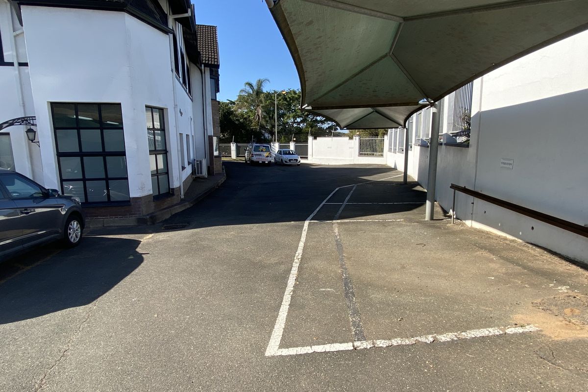 Commercial exterior rear parking area featuring a shade cloth carport structure and paved asphalt surface with perimeter security fencing.