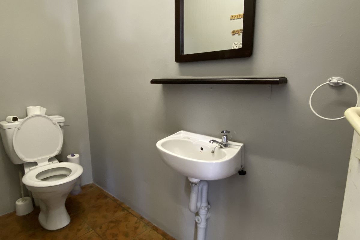 A functional commercial bathroom featuring a wall-mounted basin, toilet, and tiled flooring with neutral wall finishes.