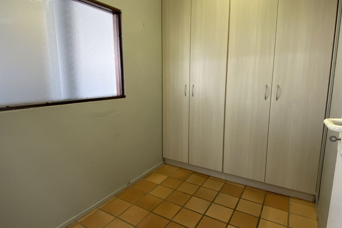 A functional bedroom space featuring built-in cupboards, tiled flooring, and a frosted glass window, offering a blank canvas for potential updates.