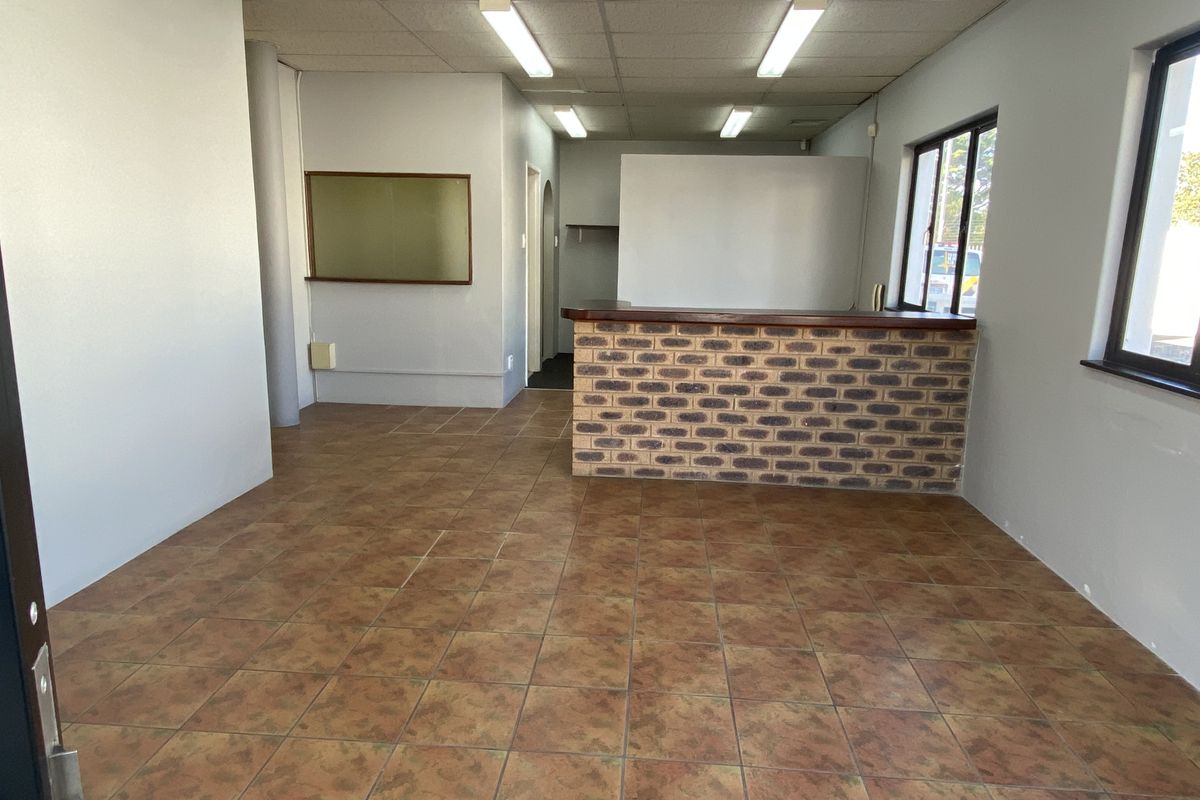 An open-plan commercial office space featuring tiled flooring, a brick reception counter, and functional drop ceiling lighting.