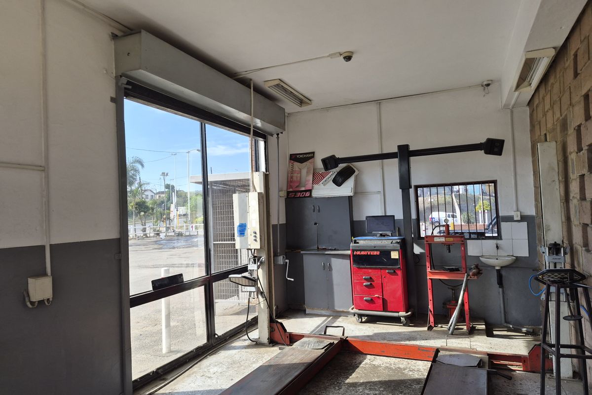 A functional automotive workshop bay featuring a built-in vehicle lift, roller shutter door, and a small wall-mounted basin for utility use.