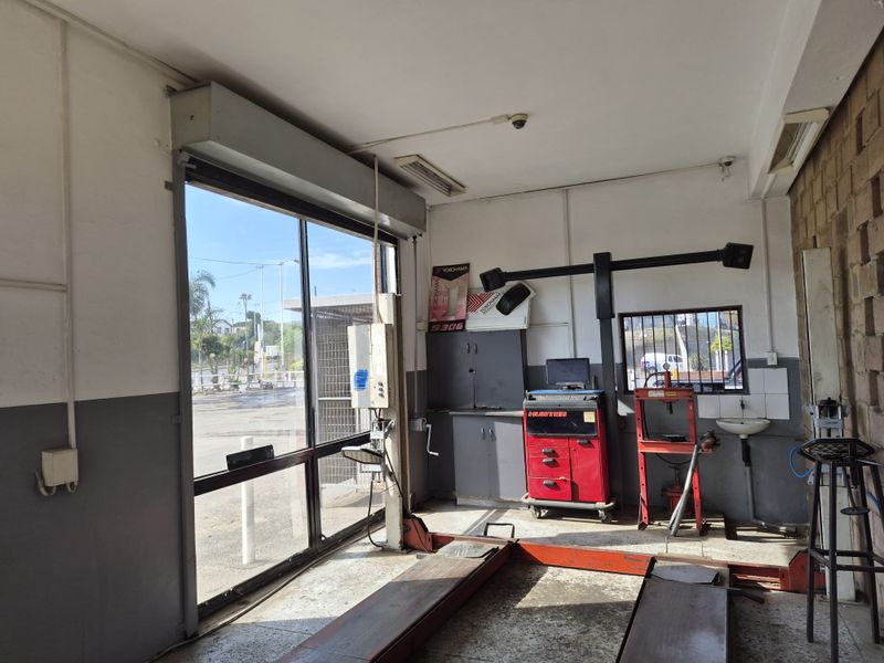 A functional automotive workshop bay featuring a built-in vehicle lift, roller shutter door, and a small wall-mounted basin for utility use.