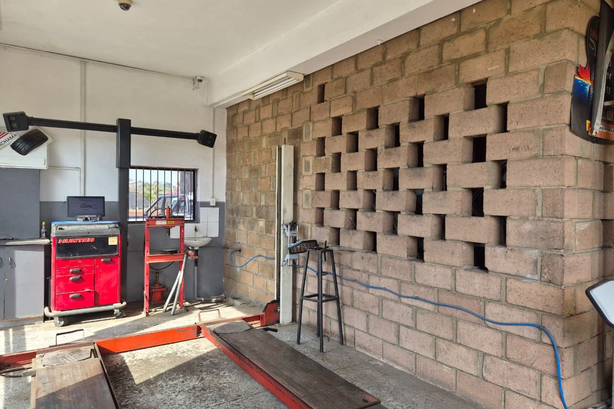Functional workshop garage space featuring a vehicle lift, exposed brick wall, and integrated wash basin, suitable for automotive service operations.