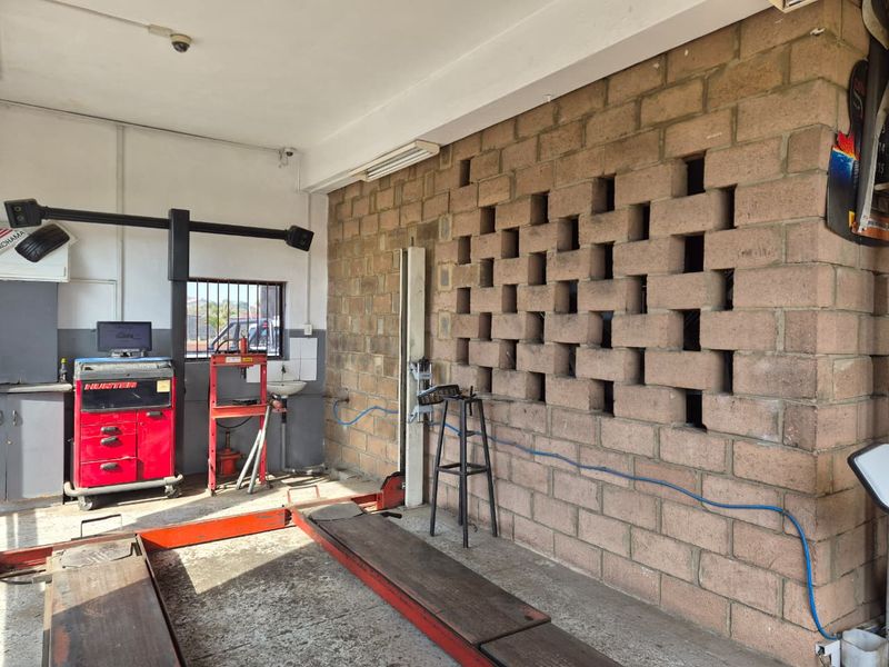 Functional workshop garage space featuring a vehicle lift, exposed brick wall, and integrated wash basin, suitable for automotive service operations.