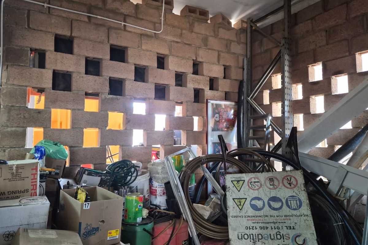 A utility storage area featuring a distinctive breeze block wall, exposed electrical conduit, and industrial metal shelving.
