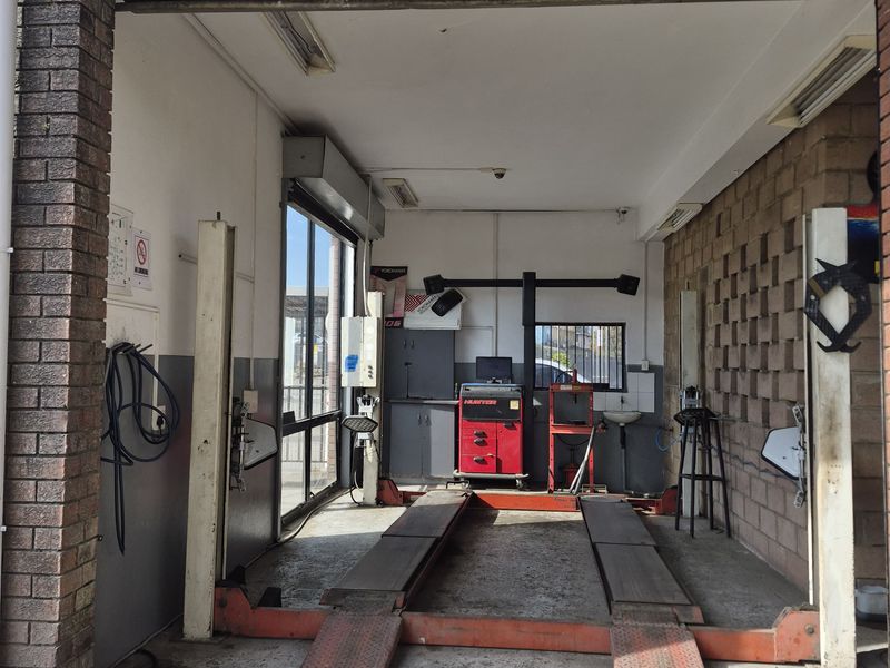 A functional automotive workshop bay featuring a built-in vehicle lift, exposed brick walls, and integrated lighting, suitable for professional mechanical services.